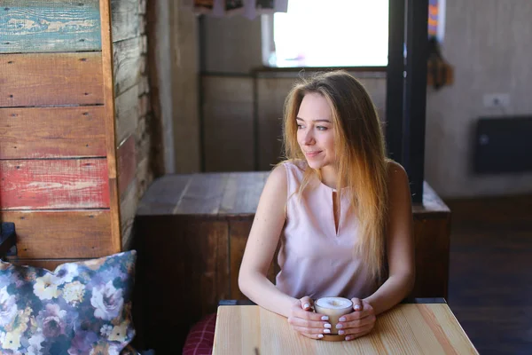 Kobieta siedzi w przytulnej kawiarni z filiżanki cappuccino i pozowanie do zdjęć. — Zdjęcie stockowe
