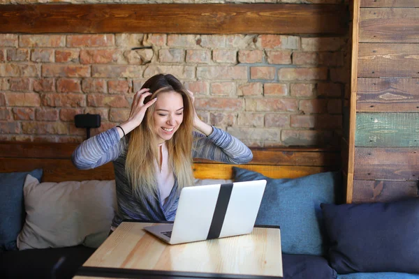 Young woman sitting in cozy coffee house near table with glass cup of cappuccino and chatting using laptop. — Stock Photo, Image