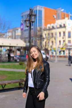 Şehirde yürüyüş ve deri ceket giyiyor neşeli kadın kişi.