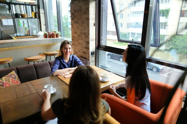 Frauen sitzen im gemütlichen Café, lächeln und trinken Kaffee. — Stockfoto