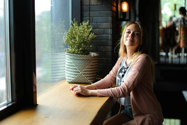 カフェの窓のそばに座って、夢を見ている若い女性. — ストック写真