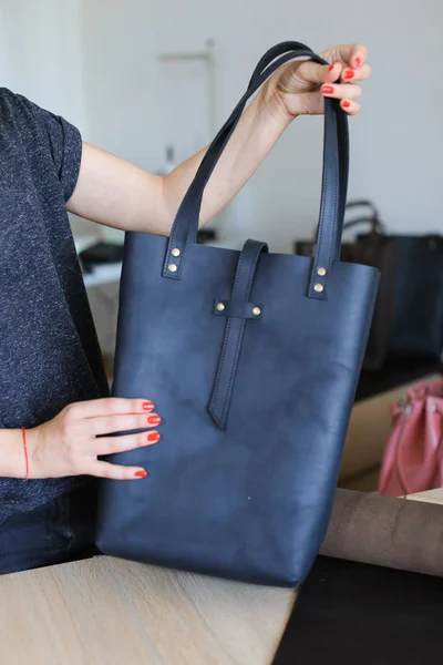 Frau mit roten Nägeln hält schwarze Frau handgemachte Lederhandtasche im Atelier. — Stockfoto