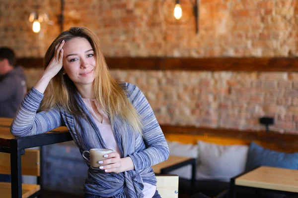 Zadowolony dziewczyna siedzi w pobliżu tabeli filiżankę cappuccino w przytulnej kawiarni z niezwykłym wnętrzu. — Zdjęcie stockowe