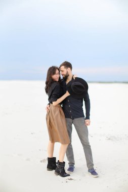 Mutlu genç gülümseyen etek giyen ve şapka, kış kar arka plan tutmak beyaz kadın hugginng adam.