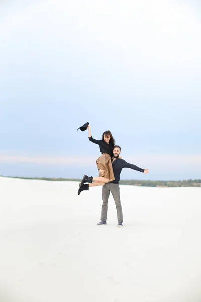 Joven feliz chico recogiendo en manos chica usando falda en blanco nieve fondo . — Foto de Stock