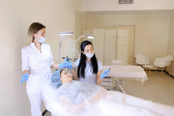 Косметолог делает постоянный макияж для женщины в кабинете с медсестрой . — стоковое фото