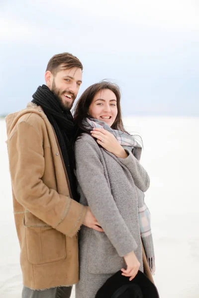 Glad leende man kramas kvinnliga person klädd i grå kappa och halsduk, vit vinter monofoniska bakgrund. — Stockfoto