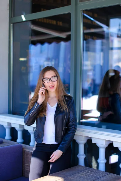 Mujer bonita en gafas hablando por teléfono inteligente en la cafetería de la calle . — Foto de Stock