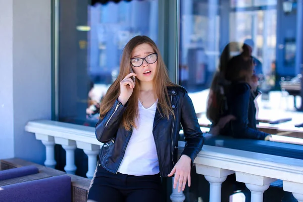 Menina feliz vestindo óculos e falando por smartphone no café de rua . — Fotografia de Stock
