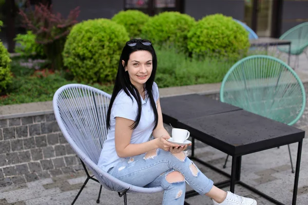 Gladden pessoa feminina sentada na cadeira no café perto de plantas verdes e beber café . — Fotografia de Stock