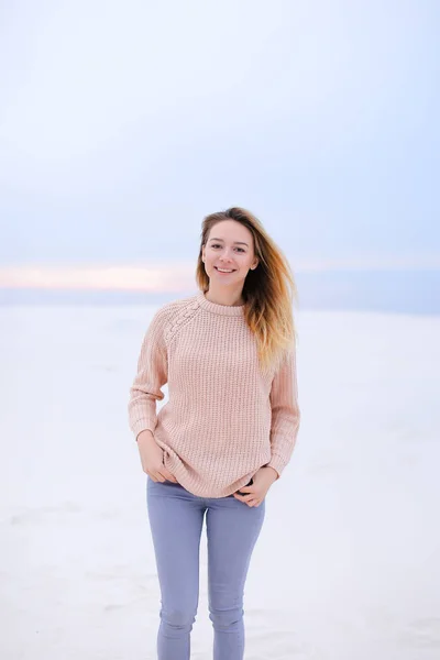 Happy girl wearing pink sweater and jeans standing in white winter background. — Stock Photo, Image