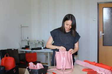 Pembe el yapımı deri kadın çanta ve cüzdan ile bir atölye duran kadın.