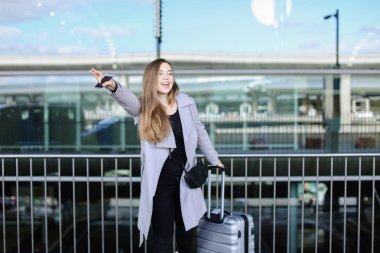 Genç kız yükseltilmiş el, valiz ve smartpone yakınındaki taksi durdurma.