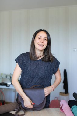 Atelier, kahverengi deri el yapımı çanta ile duran genç kadın.