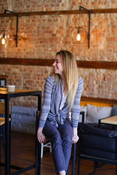 Zadowolony dziewczyna siedzi w pobliżu tabeli w przytulnej kawiarni z niezwykłym wnętrzu. — Zdjęcie stockowe