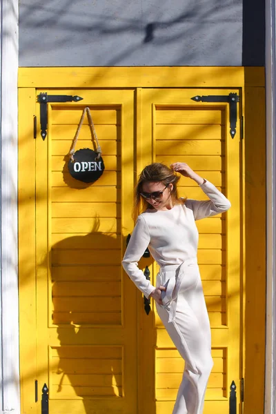 Dame à la mode portant costume blanc debout près de la porte du café dans les rayons du soleil . — Photo
