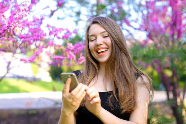 Sonriente persona femenina usando smartphone en el parque con fondo de flor . — Foto de Stock