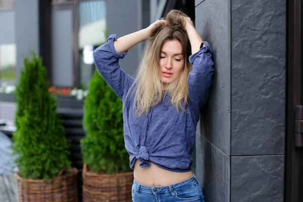 블루 셔츠와 서 청바지를 입고 금발 여성 모델 구축 및 녹색 식물을 가까이. — 스톡 사진