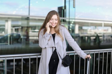 Valiz ile ayakta ve yakınındaki smartpone tarafından konuşurken Kafkas genç kadın.