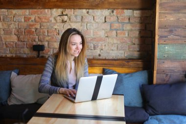 Rahat coffee House tablo cam fincan kapuçino ve dizüstü bilgisayar kullanarak sohbet ile yakın oturan genç kadın.