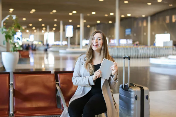 Młoda kobieta kaukaski, korzystanie z Internetu przez tablet w hali lotniska w pobliżu walizka. — Zdjęcie stockowe