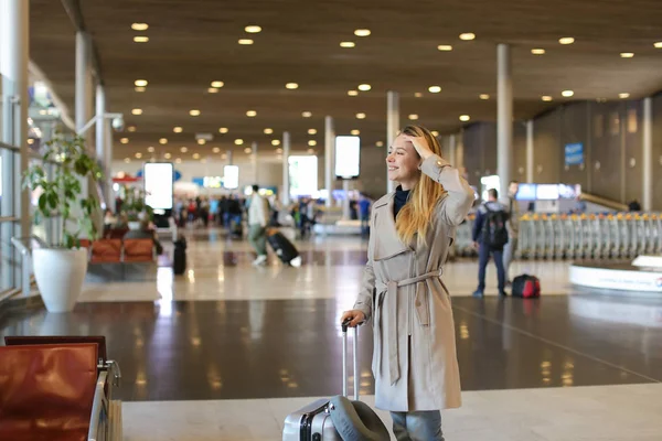 Kaukaski dziewczyny spaceru w Lotnisko w poczekalni z valise i na sobie szary płaszcz. — Zdjęcie stockowe