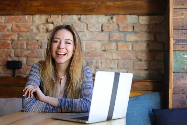 Mujer linda usando el ordenador portátil en la cafetería con fondo de pared de ladrillo . — Foto de Stock