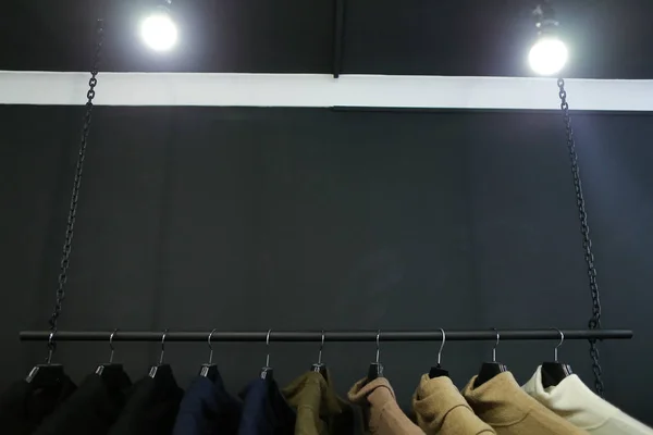 Ramínka s oblečením a lampy v šatníku v černém pozadí. — Stock fotografie