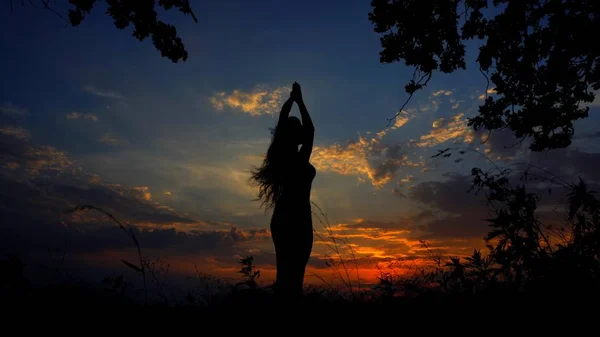 Female silhouette doing yoga and meditating in evening sky background.