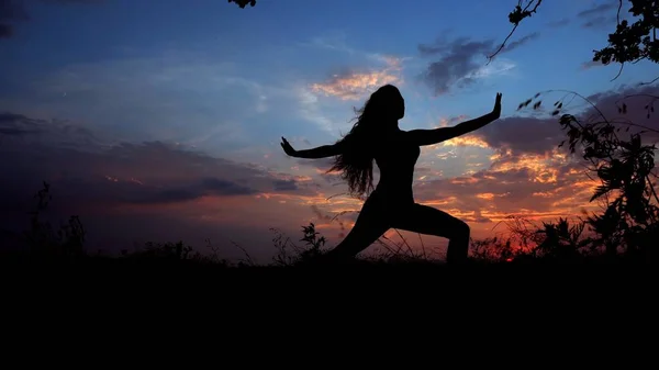 Woman black shadow doing yoga, female silhouette in evening sky background.