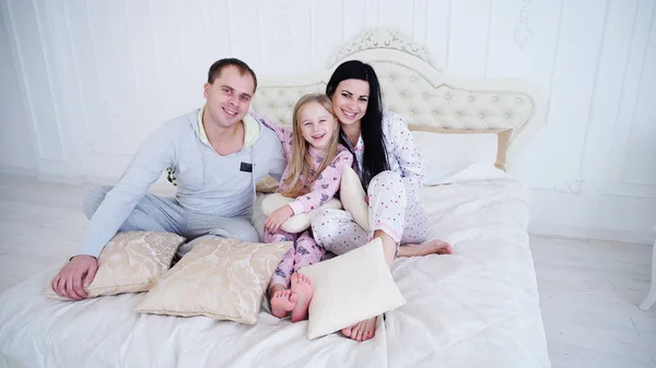 Kaukasische ouders en dochtertje zittend op bed in de ochtend, het dragen van pyjama 's. — Stockfoto