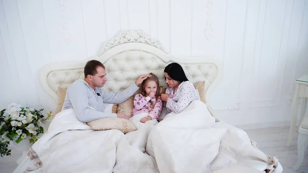 Małą córeczkę, kaszel i leżąc w łóżku z rodzicami w rano. — Zdjęcie stockowe