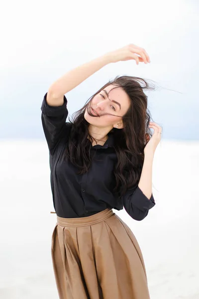 Young smiling woman with raised hands wearing black shirt and skirt standing in white winter background.