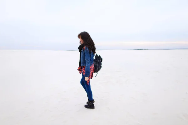 Jovem caucasiana caminhando sobre fundo de neve e vestindo jeans com saco . — Fotografia de Stock