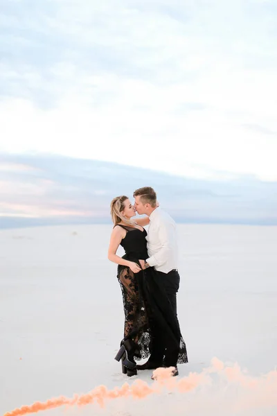 Menina jovem vestindo vestido preto transparente beijando o homem no campo nevado . — Fotografia de Stock