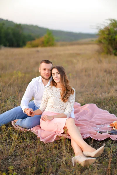 Jonge mooie vrouw en man zitten op roze ruit op de natuur. — Stockfoto