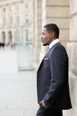 Siyah takım elbiseli ve binanın yanında duran Afro-Amerikan adam..