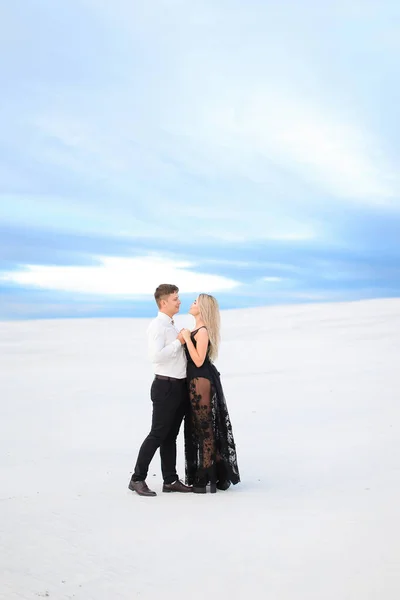 Young man in white shirt hugging woman wearing black dress in winter steppe. — Stockfoto