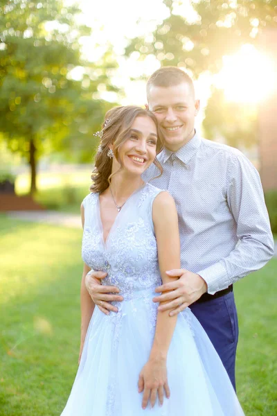 Joyeux marié souriant embrassant la mariée dans le parc, les rayons du soleil . — Photo