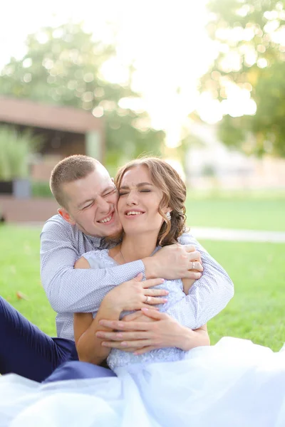 Happy groom hugging nice bride and sitting on grass in garden. — Stock Photo, Image