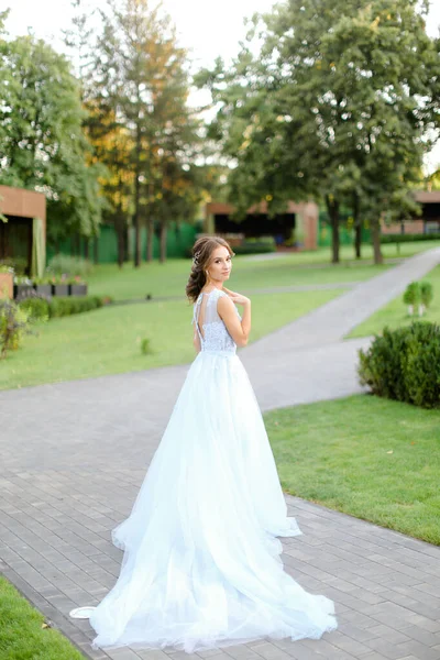 Λευκή όμορφη νύφη στέκεται στον κήπο και φοράει μακρύ λευκό φόρεμα. — Φωτογραφία Αρχείου