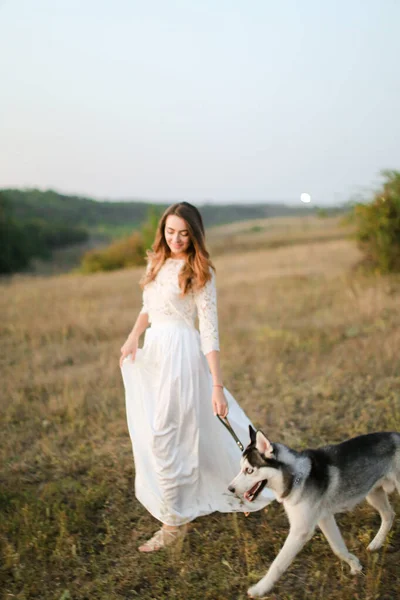 Caucasian european bride walking in steppe with dog and wearing white dress. — Stock Photo, Image