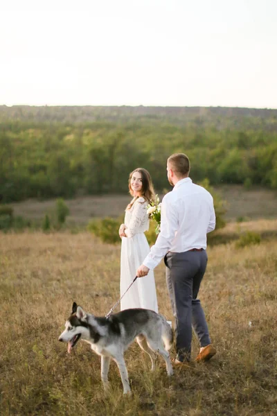 Sposo e sposa felice passeggiando in steppa con cane husky . — Foto Stock