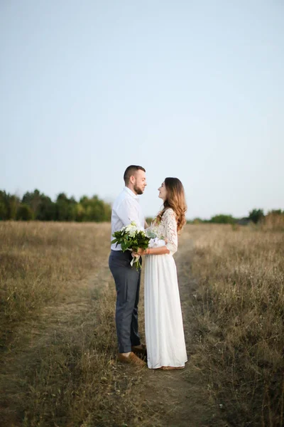 Damat bozkır arka planında bir buket çiçekle geline sarılıyor.. — Stok fotoğraf