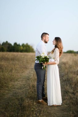 Damat bozkır arka planında bir buket çiçekle güzel gelini kucaklıyor..