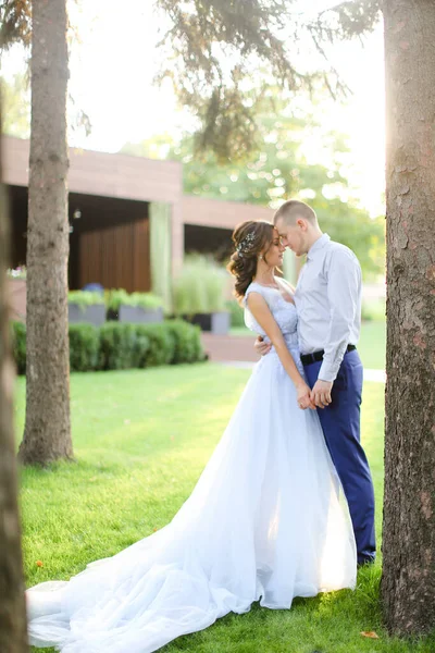 Caucasiano jovem noiva beijando com noivo no parque e vestindo vestido branco . — Fotografia de Stock