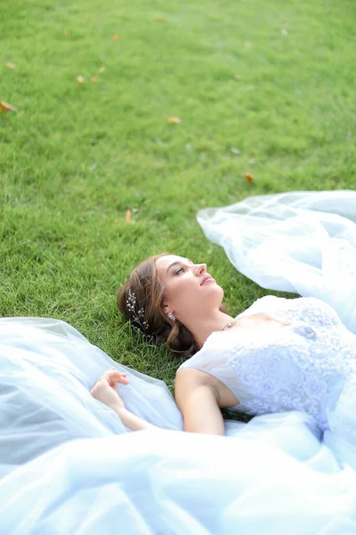 Mariée innocente allongée sur l'herbe en oark et portant une robe blanche . — Photo