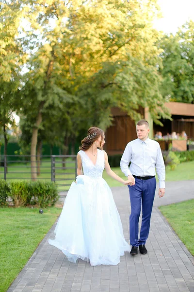 Junge Braut spaziert mit kaukasischem Bräutigam im Garten. — Stockfoto