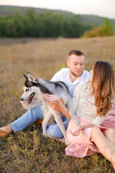 Young caucasian woman and man sitting on gras with husky. — Stockfoto