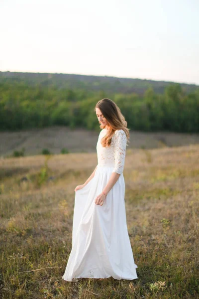 Caucasian young bride standing in steppe and wearing white dress. — Stock Photo, Image